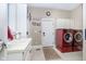 Convenient laundry room with modern red washer/dryer, sink, white cabinetry and neutral tile floor at 5030 Nightshade Ln, Noblesville, IN 46062