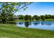 Serene pond view with lush green grass and mature trees at 10349 Gateway Dr, Brownsburg, IN 46234
