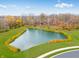 Aerial view of the pond surrounded by lush green landscaping and colorful foliage at 567 Hidden Hills Dr, Pittsboro, IN 46167