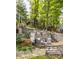 Multi-tiered outdoor living space with stone walls and patio seating, surrounded by mature trees at 7082 Muskrat Dr, Nineveh, IN 46164