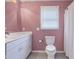 Bathroom with pink walls, white vanity, toilet, and window with blinds at 12404 Doe Ln, Indianapolis, IN 46236
