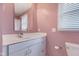 Bathroom area featuring pink walls, white cabinets, sink, mirror, and window with blinds at 12404 Doe Ln, Indianapolis, IN 46236