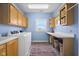 Bright laundry room featuring blue walls, overhead cabinets, washer, dryer, and colorful rug at 5895 W 265 N, Columbus, IN 47201