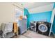 A laundry room featuring blue walls, a gray cabinet, a window, and modern washer and dryer units at 14402 Wolverton Way, Fishers, IN 46037
