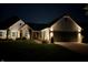 Night view of home exterior with brick and siding, illuminated landscaping, and a two-car garage at 9046 Pinecreek Ct, Indianapolis, IN 46256