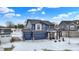 Two-story blue home featuring a three-car garage, stone accents, and a welcoming porch under a bright sky in the winter season at 5461 Oak Knoll Dr, Whitestown, IN 46075