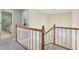 A well-lit upper hallway featuring wood railing, neutral carpeting, and a view of the entry below at 7238 River Birch Ln, Indianapolis, IN 46236