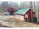 An exterior view of a red home and shed, both with green roofs, nestled among bare trees in a wooded area at 9464 N State Rd 135, Morgantown, IN 46160