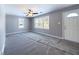 Spacious living room featuring new gray carpet, gray walls, a ceiling fan, a large window, and a white front door at 1235 Indiana Ave, Anderson, IN 46012