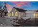 Charming home exterior featuring stone accents, a two-car garage, and winter landscaping at dusk at 7415 Chapel Villas Dr # D, Indianapolis, IN 46214