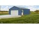 A blue storage garage featuring a white garage door and an entry door on a well maintained lawn at 8225 W 825 N, Thorntown, IN 46071