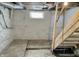 Unfinished basement with concrete floor, painted walls, and wooden stairs, illuminated by a single bulb at 210 S West St, Paragon, IN 46166