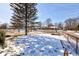 View of neighborhood from the backyard featuring a large tree, snowy lawn, and chain link fence at 4139 N Grand Ave, Indianapolis, IN 46226