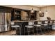 Basement bar with dark cabinetry, granite countertops, stainless steel refrigerator, and bar seating at 11573 Bent Tree Ct, Zionsville, IN 46077