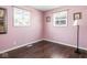 A cozy bedroom with pink walls, hardwood floors, and natural light from two windows at 1420 E Market St, Indianapolis, IN 46201