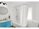 Bright bathroom with a clean aesthetic, featuring a bathtub with shower, a sleek round mirror, and a blue vanity at 2401 N Olney St, Indianapolis, IN 46218