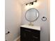Bathroom vanity with a black cabinet, gold hardware, a round mirror, and modern fixtures at 11708 Rolling Springs Dr, Carmel, IN 46033