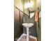 Stylish half bathroom with a pedestal sink, round mirror, and modern lighting fixture at 1381 Delacorte Cir, Shelbyville, IN 46176