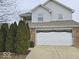 Two-story home featuring a brick and vinyl facade, attached two-car garage, and mature evergreen trees at 6114 Arrowhead Dr, Anderson, IN 46013