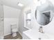 Bright bathroom featuring white vanity and commode, a window, and round mirror at 516 W Washington St, Lebanon, IN 46052
