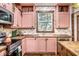 Charming kitchen featuring pink cabinets, wood countertops, stylish backsplash and modern stainless steel appliances at 1647 N Tacoma Ave, Indianapolis, IN 46218
