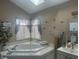 Corner bathtub in a bathroom with ample light, tiled deck, privacy shutters, and decorative accents at 4418 Tarragon Dr, Indianapolis, IN 46237
