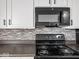 Close up of kitchen with black stove top and microwave surrounded by white cabinets and tile backsplash at 718 Indiana Ave, Shelbyville, IN 46176