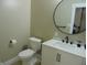 A bathroom featuring toilet and vanity with quartz countertop and round mirror at 2528 Carrollton Ave, Indianapolis, IN 46205