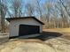 Detached garage with dark-colored door and tan siding is set in a wooded yard at 8468 N Baltimore Rd, Monrovia, IN 46157