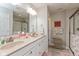 A bright bathroom features double sinks, a large mirror, and a glass-enclosed shower with neutral walls and floral accents at 6400 Woodland Ln, McCordsville, IN 46055