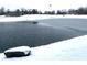 Winter view of home's pond covered in partial ice with luxury home and flagpole in the background at 9615 N County Road 150 E Rd, Pittsboro, IN 46167