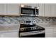 Close up view of stainless stove, microwave and decorative tile backsplash at 5402 Basin Park Dr, Indianapolis, IN 46239