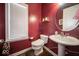Stylish powder room with a pedestal sink, round mirror, and a red accent wall at 7239 Bellini Ln, Indianapolis, IN 46259