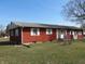 Exterior shot of a long, red single-story home with white trim and ample lawn space at 210 Evergreen St, Morgantown, IN 46160