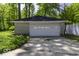 A detached garage with a white door sits on a concrete slab, surrounded by green foliage and a partial fence at 6204 S Madison Ave, Indianapolis, IN 46227