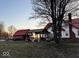 Backyard view of a white farmhouse with a red roof next to a covered outdoor seating and BBQ area at 8089 W Old State Road 67, Paragon, IN 46166