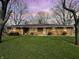 Charming single-story brick home with a spacious front yard and mature trees under a twilight sky at 3008 Nichol Ave, Anderson, IN 46011