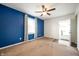 Living room features blue accent wall, neutral carpet, ceiling fan and exterior door at 3225 S Rybolt Ave, Indianapolis, IN 46221