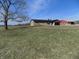 Scenic view of a ranch home surrounded by greenery, a large tree, and a red building in the background at 10966 W State Road 142, Quincy, IN 47456