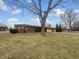 Brick ranch-style home featuring an attached garage and a spacious front yard with mature trees under a blue sky at 3509 River Bluff Rd, Anderson, IN 46012