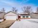 Charming single-story home with a red door and attached garage surrounded by a snow-covered yard and bare trees at 3936 Par Dr, Indianapolis, IN 46268