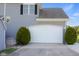 Attached two-car garage with a clean, modern door, complemented by manicured shrubs and a paved driveway at 7845 W Hillside Dr, Columbus, IN 47201