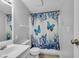 Bright bathroom with single sink vanity, commode, and shower with blue floral butterfly shower curtain at 2305 S Rybolt Ave, Indianapolis, IN 46241