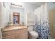 Bathroom featuring neutral vanity, large mirror, toilet, shower with blue accent curtain, and a small shelf above toilet at 10212 Ironway Dr, Indianapolis, IN 46239