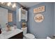 Cozy bathroom featuring a white vanity, toilet, and blue-gray walls with decorative accents at 7383 Poppyseed Dr, Indianapolis, IN 46237