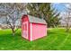 A backyard shed is painted red with a gray roof and situated on a lush green lawn near trees at 222 Wellington Pkwy, Noblesville, IN 46060