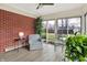 Sunroom with a cozy blue armchair, brick wall, and views of the landscaped backyard at 6537 Grosvenor Pl, Indianapolis, IN 46220