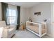 This charming Bedroom features a white crib, rocker, and natural light from the window at 9184 Anthem Ave, Plainfield, IN 46168