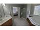 Bright bathroom with a double vanity, soaking tub, glass block window, and open doorway to the bedroom at 452 Twin Oaks Dr, Carmel, IN 46032