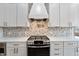 Close-up of a kitchen stove with white cabinetry, stone backsplash and stainless steel appliances at 5123 Oak Ridge Pl, Columbus, IN 47201